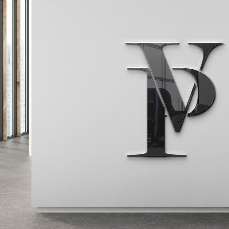 Sleek, polished 'PV' monogram logo mounted on a white wall in a modern interior space with large windows.