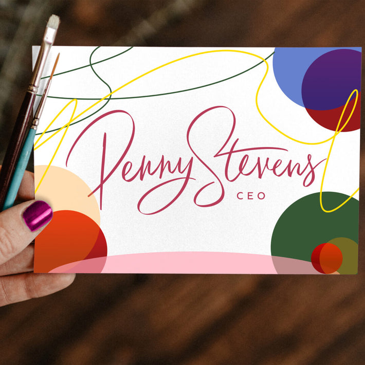 Handwritten 'Penny Stevens' logo with 'CEO' title, surrounded by colorful abstract shapes, held in a person's hand with a paintbrush nearby.